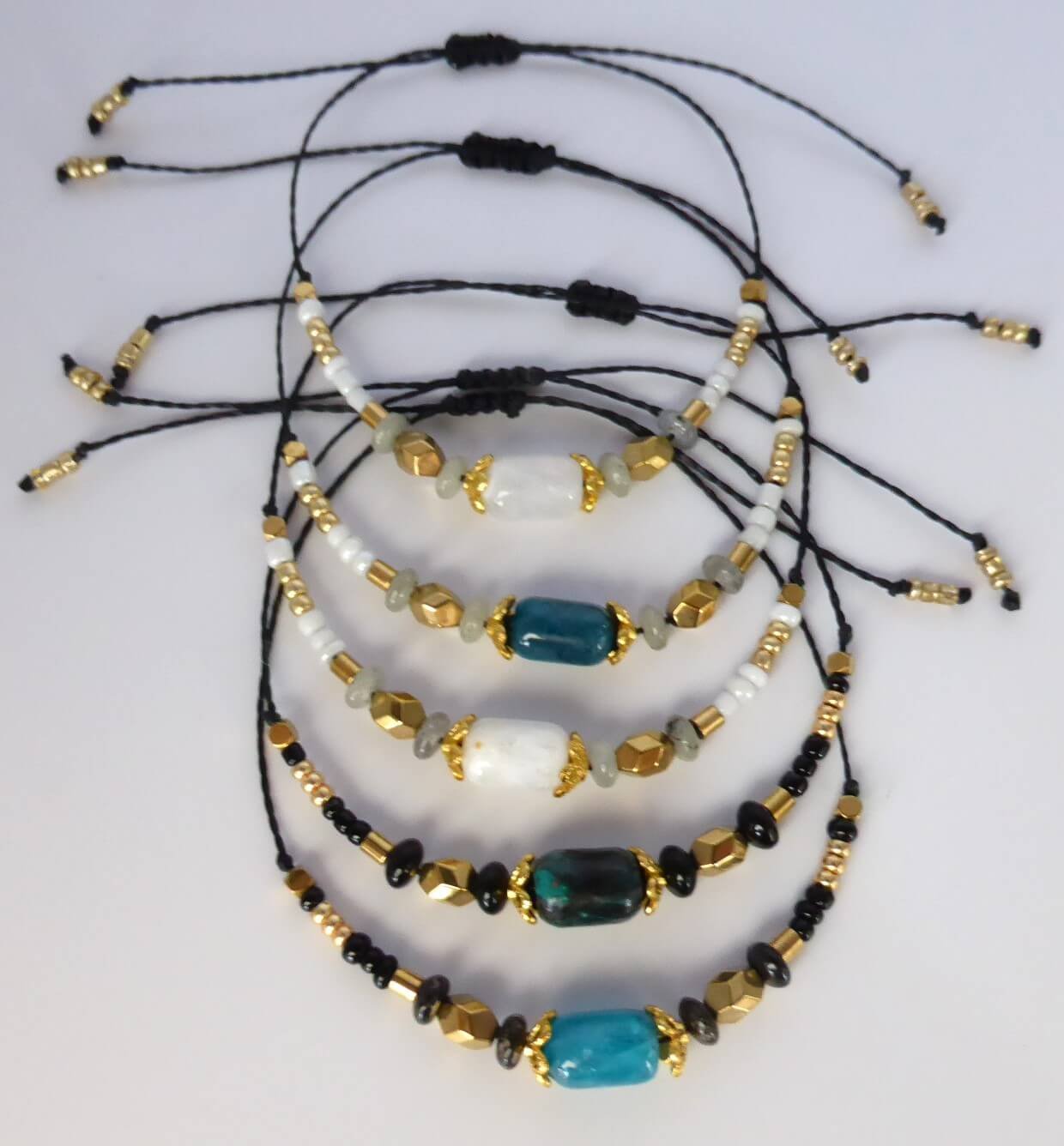 Bracelet Lindo avec perles en pierre naturelle gemme, perles en hématite doré et perles de rocaille noire. Les perles sont montées sur un cordon ciré terminé par des perles de rocaille dorées.