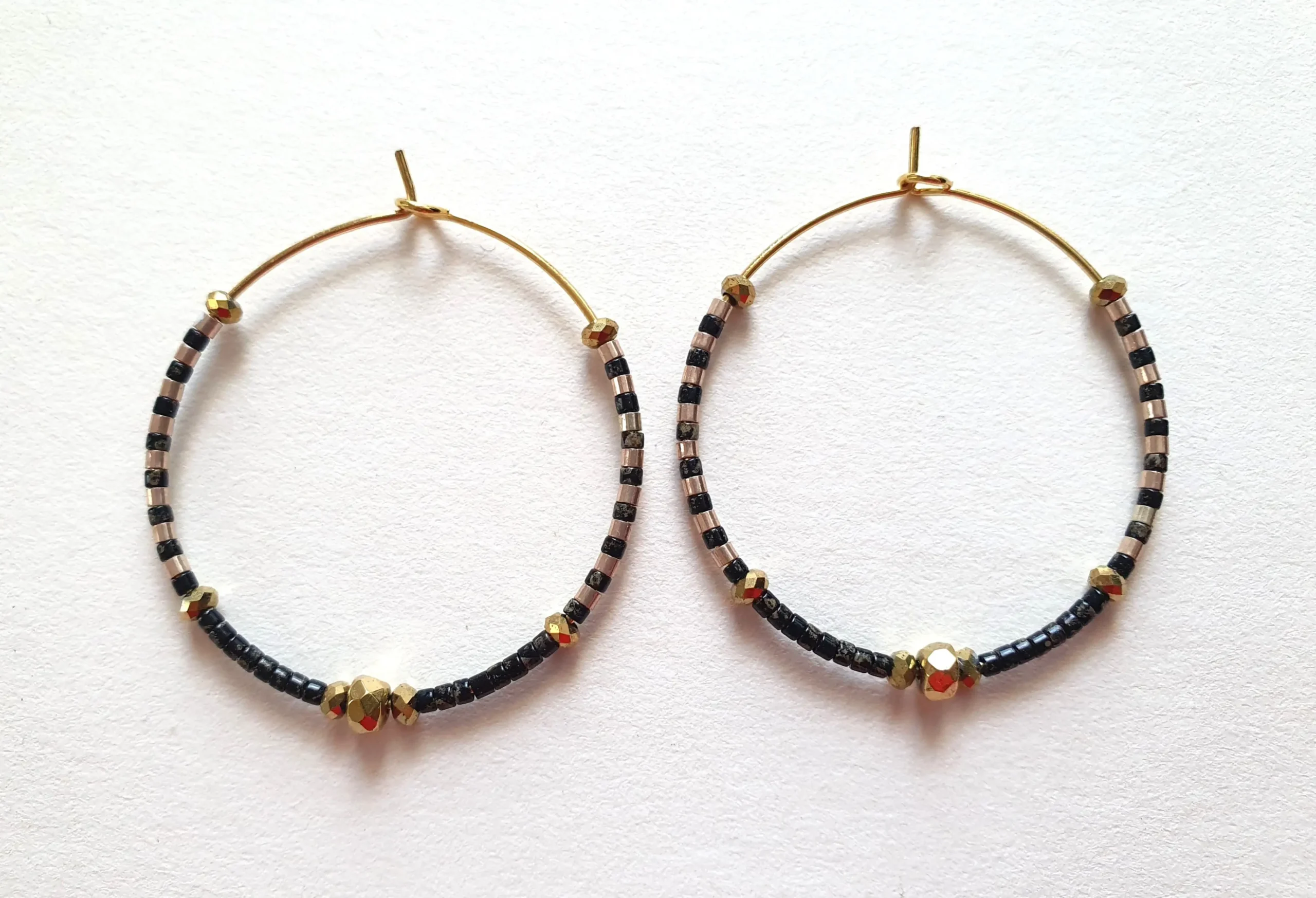 Boucles d'oreilles créoles en perles noires picasso. Vue à plat.