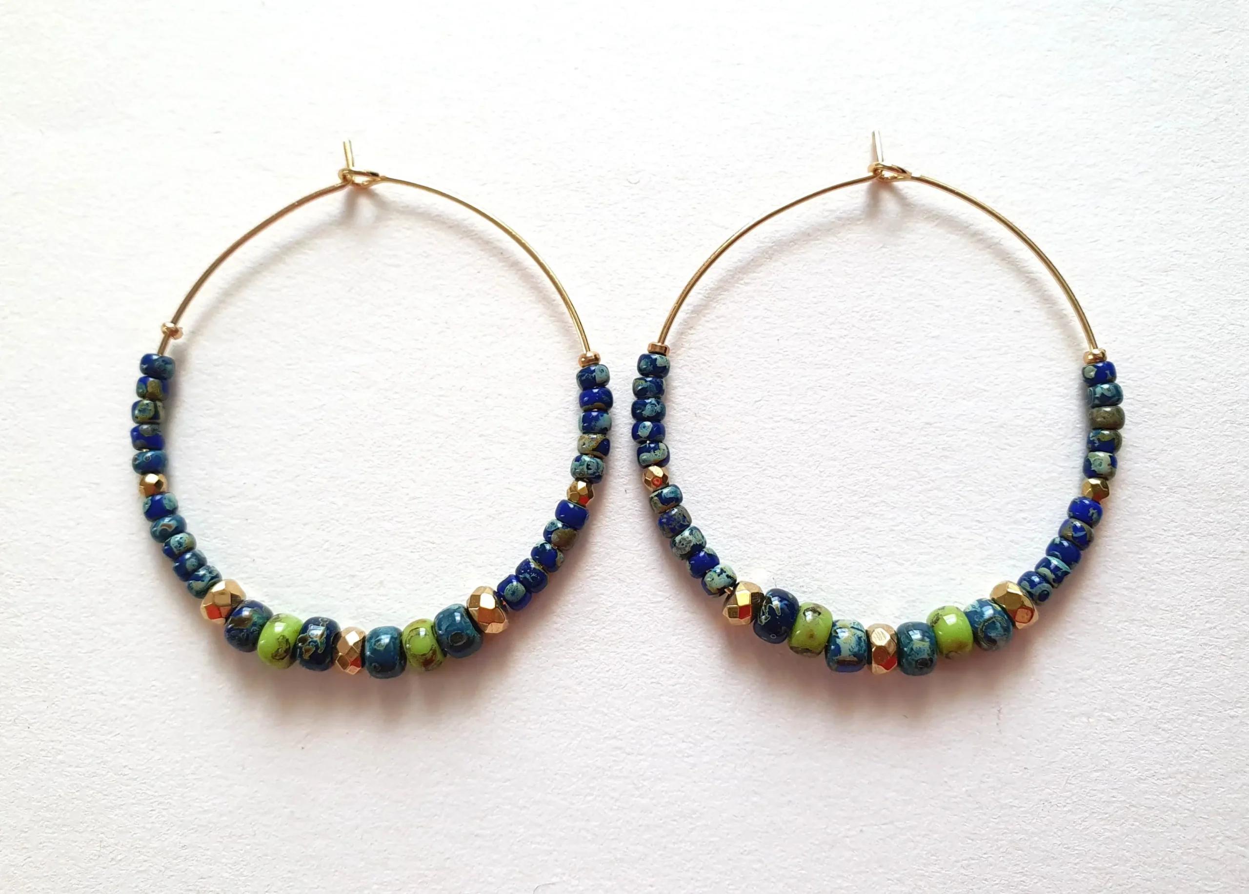 Boucles d'oreilles créoles en perles bleues et vertes anis picasso. Vue à plat.