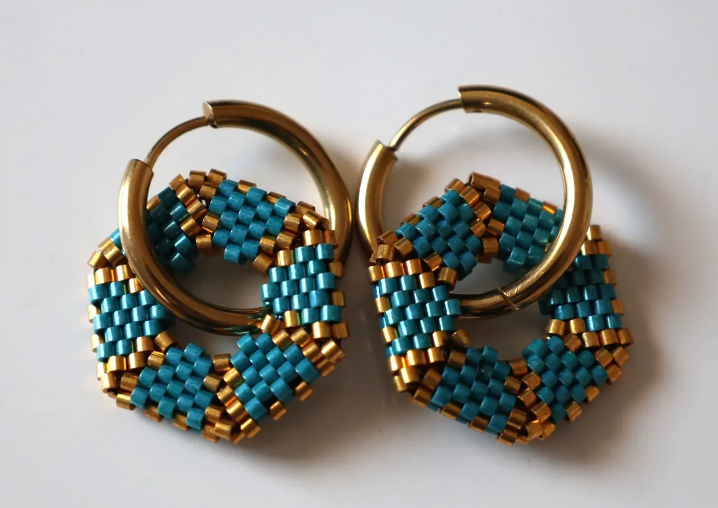 Boucles d'oreilles créoles avec pampille hexagonale en perles miyuki tissées bleues et dorées. Vue à plat